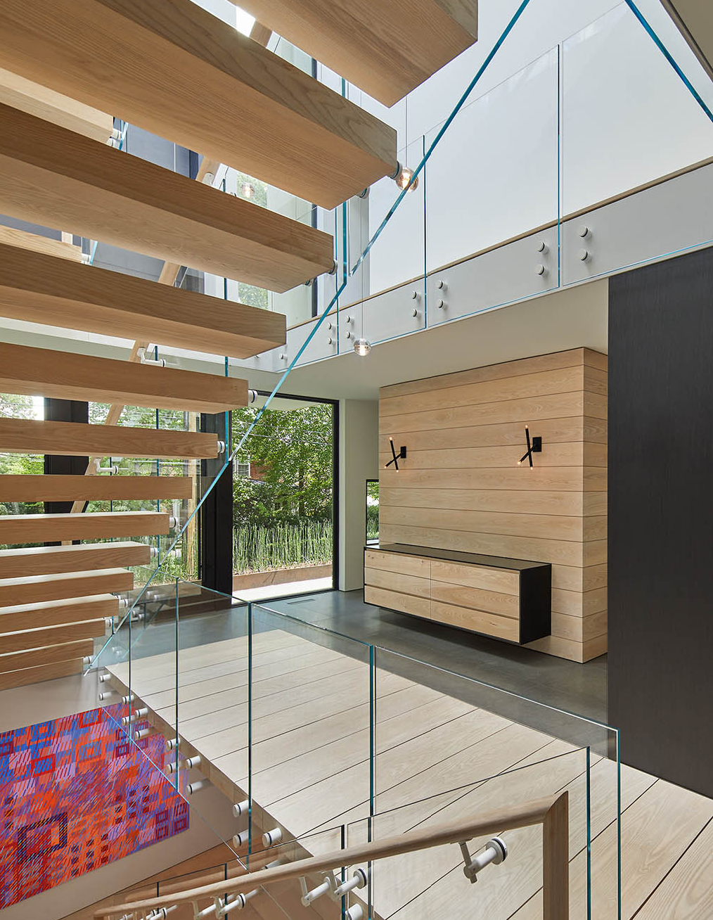 Photo of modern interior with glass staircase and light colored wood cabinets 