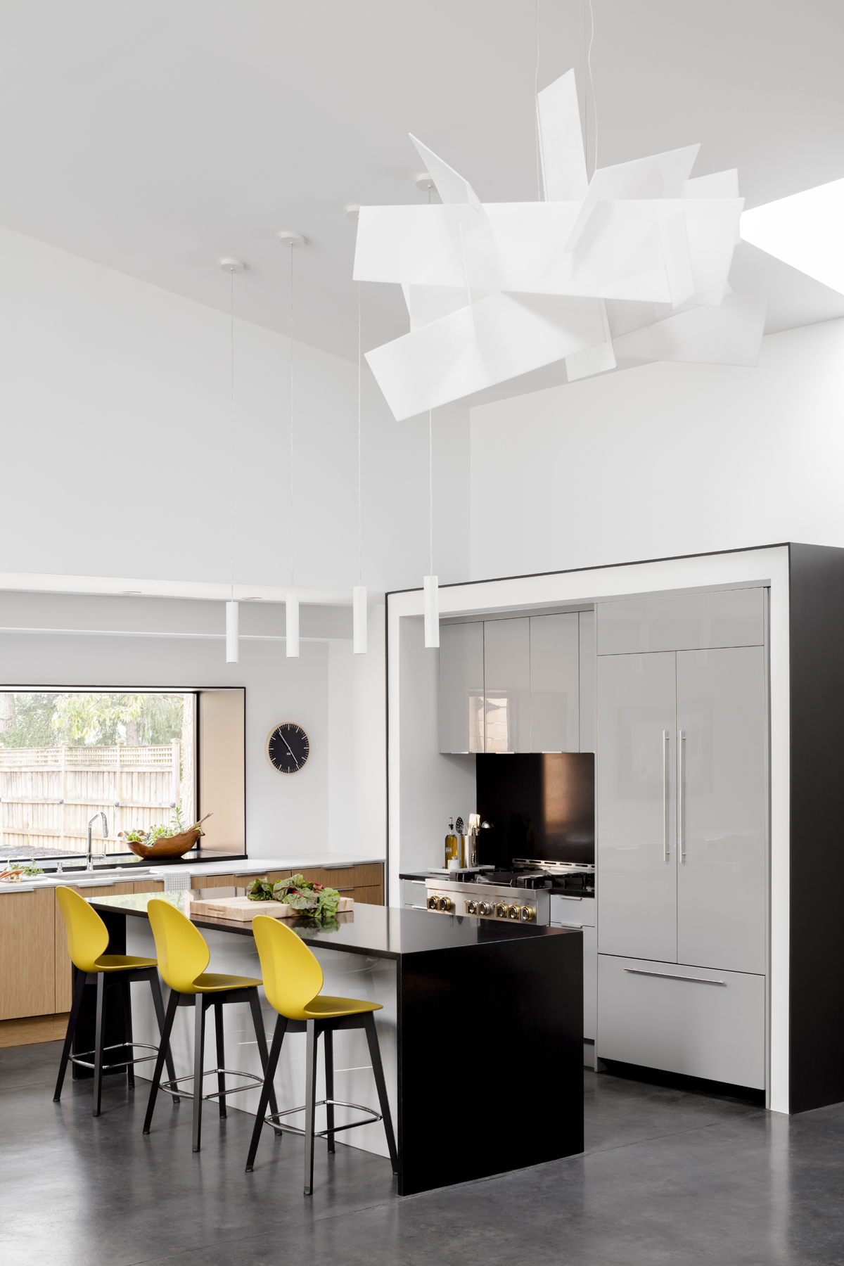 Modern kitchen with concrete floors, glossy grey cabinetry and sculptural light fixture